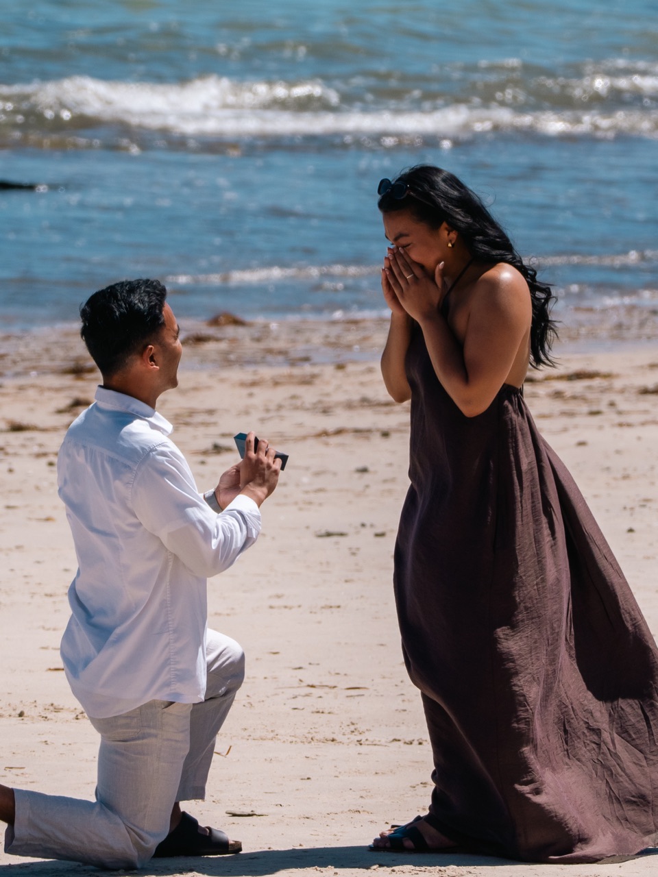Beach proposal — he kneels with the ring as she covers her face in surprise
