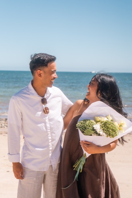 Newly engaged couple laughing with a bouquet on an Adelaide beach