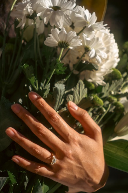 Hand with engagement ring resting on a white chrysanthemum bouquet