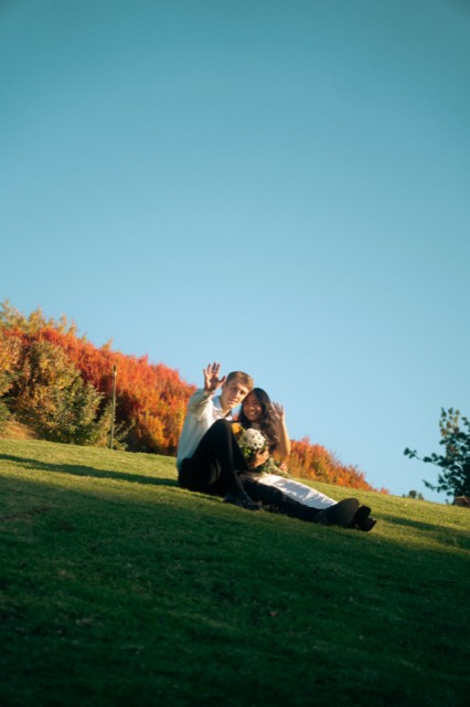 Couple sitting on a sunlit hillside at golden hour, waving